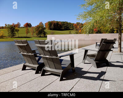 Entspannende Poolszene mit drei klassischen Adirondack-Stühlen, die für Komfort ausgelegt sind. Klare Linien und ruhiges blaues Wasser schaffen eine luxuriöse Sommeratmosphäre. Stockfoto