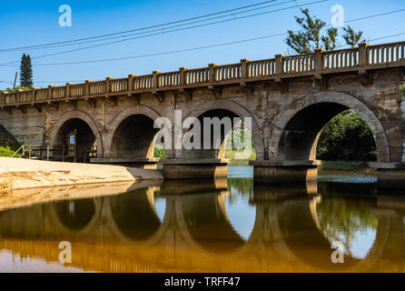 Alte Eisenbahnbrücke mit Spiegelbild im Wasser auf einem hellen Sommer morgens auf den Strand in Durban, Südafrika Stockfoto