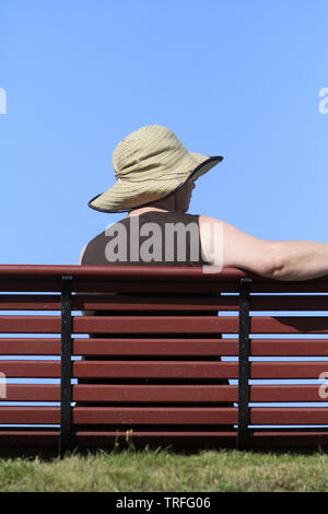 Femme wichtige un chapeau assise sur un Banc. Stockfoto