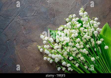 Maiglöckchen Blumenstrauß auf dunklen braunen Hintergrund. Ansicht von oben. Stockfoto