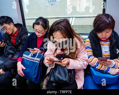 SHANGHAI, China - 12 MAR 2019 - eine Reihe von Pendlern auf der Shanghai Metro alle auf ihren Smartphones. China hat eine extrem hohe Rate von Smartphone markieren Stockfoto