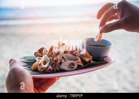 Gegrillter Tintenfisch am Strand Meer Hintergrund/Scheibe der Squid auf Platte mit Thai Seafood Soße auf der Hand Stockfoto