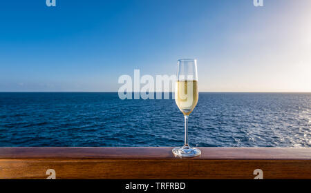 Ein Glas Champagner auf einer hölzernen Geländer eines Kreuzfahrtschiffes. Meer Hintergrund. Stockfoto