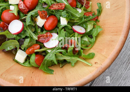 Blick von oben auf eine Holzschüssel mit frisch gemixtem Salat: Rucola, Kirschtomaten, Mozzarella-Käse, Rettich. Stockfoto