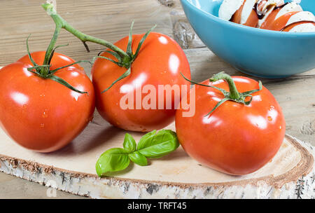 Tomaten und frischen Blätter Basilikum auf Holz. Caprese Salat im Hintergrund. Stockfoto