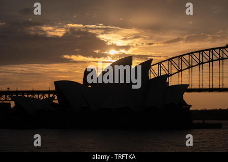 Das Sydney Opera House und der Sydney Harbour Bridge in Silhouette gegen einen orange Sonnenuntergang gezeigt. Stockfoto