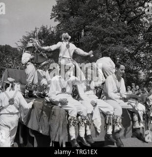 1950, historische, an einem heissen Sommertag, einer Gruppe von männlichen Morris Dancers spielen auf einem Karneval schweben, mit drei von Ihnen eine Pause vom Tanzen ausruhen und eine Zigarette, England, UK zu genießen. Morris tanzen ist ein traditioneller englischer Volkstanz und ein wichtiger Teil der Sommer Museen und Monumente, Stockfoto