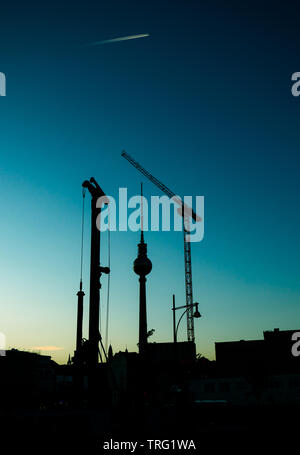 Der Berliner Fernsehturm bei Sonnenuntergang durch den Bau von Kränen gerahmt Stockfoto