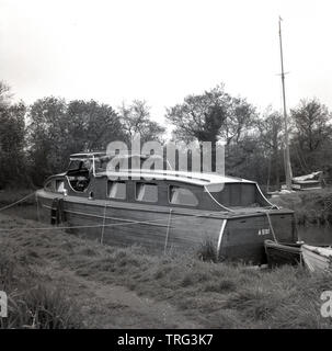 1950, historische, ein Mann auf einer hölzernen Cabin Cruiser Boat, neben einem flußufer auf der Themse in der Nähe von Oxford, England, UK. Stockfoto