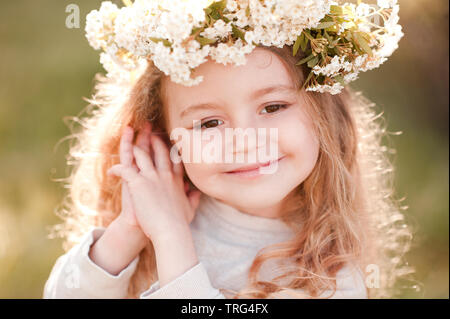 Lächelnden Mädchen 4-5 Jahre alten tragen Blume Kopfbügel im sonnigen Licht im Freien. Sommer Portrait von Kind. Posing über grüne Natur Hintergrund. Stockfoto