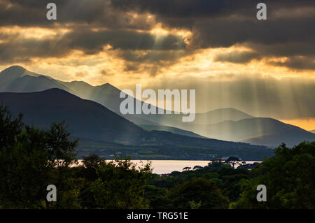 Crepuscular Strahlen und Wellen von Sonnenlicht, die durch Lücken in dramatischen Wolken über Carrauntoohil und Macgillycuddy's Reeks, County Kerry, Irland Stockfoto