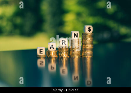 Verdienen und Geld ausgeben. Würfel Form das Wort 'verdienen' auf Stapel von Münzen platziert. Die Reflexion zeigt Pend das Wort'. Stockfoto