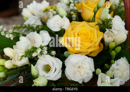 Verlust eines geliebten Menschen, ein Blumenkorb, Holz- trug, der Lilly im Tal, Convallaria majalis und gelbe Rosen mit leeren Familie Stuhl im Hintergrund Stockfoto