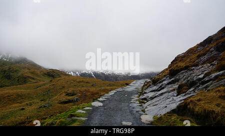 Stein Weg entlang ein beeindruckender Aussicht, durch gesättigte Gras, schönen Berge und einem nebligen Himmel - während einer Wanderung am Snowdon im Winter gefangen umgeben ( Stockfoto