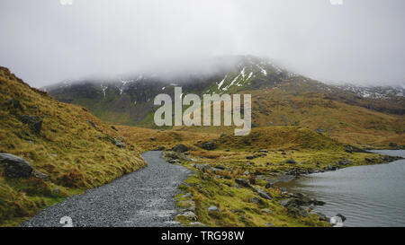 Atemberaubende Landschaft mit nebligen Himmel, schmilzt das Eis und robuste Road inmitten von wunderschönen Bergen - während einer Wanderung am Snowdon im Winter (Snowdonia Na erfasst Stockfoto