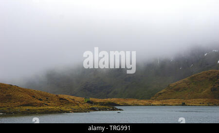 Atemberaubende Landschaft mit Nebel und Moody skies inmitten der Berge und See - während einer Wanderung am Snowdon im Winter gefangen (Snowdonia National Park, Wal Stockfoto