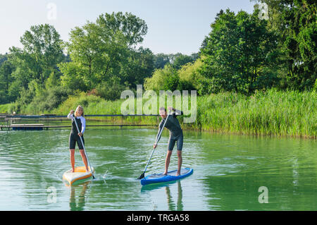 Junges Paar auf Tour mit SUP Boards an einem idyllischen See in Oberbayern Stockfoto