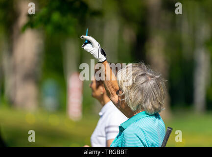 Braunschweig, Deutschland, Mai 18., 2019: Alte Frau mit dem grauen Haar auf dem Golfplatz Tests mit einem Golf-pin die Strichrichtung Stockfoto