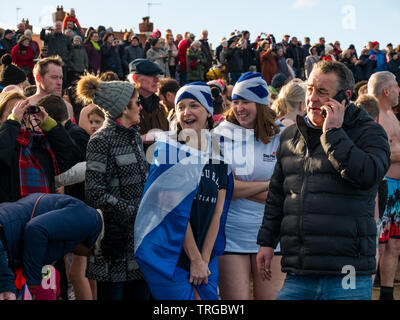 Loony Dook, Tag des Neuen Jahres: Die Menschen mutig kaltes Wasser, West Bay, Firth-of-Forth, North Berwick, East Lothian, Schottland, Großbritannien. Junge Frauen in saltire Hüte Stockfoto