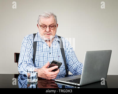 Portrait der aktiven älteren Mann mit Laptop und Smartphone zu Hause. Alter Mann mit Computer saßen und auf den Bildschirm. Altersrentner online-Modus Stockfoto