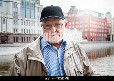 Alter Mann in Brillen und Kappe, in Moskau reisen, stehen, posieren. Ältere touristische und historische Gebäude im Hintergrund. Reiseziel Stockfoto