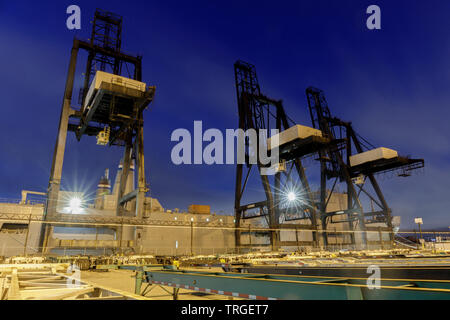 Shipping Container Krane und Lkws mit Sonnenuntergang Himmel im Hafen von Oakland. Stockfoto