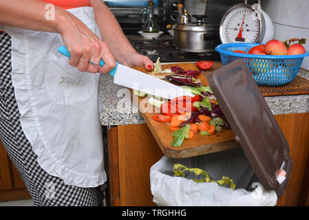 Detail einer weiblichen Hand Entsorgung der organischen Abfälle in einem geeigneten Behälter mit Küche im Hintergrund Stockfoto