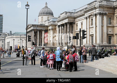 Menschen zu Fuß auf der Straße und der Gruppe der Grundschüler Schülerinnen besuchen die National Gallery Trafalgar Square in London England UK KATHY DEWITT Stockfoto