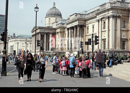 Menschen zu Fuß auf der Straße und der Gruppe der Grundschüler Schülerinnen besuchen die National Gallery Trafalgar Square in London England UK KATHY DEWITT Stockfoto