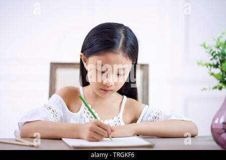 Schöne kleine asiatische Mädchen mit langen schwarzen Haaren sitzen am Schreibtisch in Ihrem Zimmer Schreiben oder Zeichnen auf Notiz Buch Stockfoto