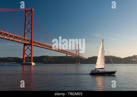 Segelboot vorbei am 25. April Brücke (Ponte 25 de Abril) über den Tejo in Lissabon, Portugal; Konzept für Reisen in Portuga Stockfoto