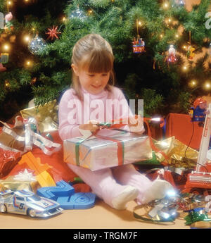 Kleines Mädchen neben einem Weihnachtsbaum Geschenke auszupacken Stockfoto