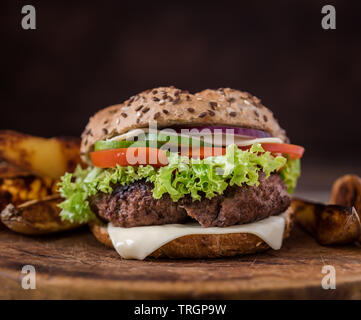 Hausgemachte Hamburger mit Käse und Salat und mit amerikanischen Kartoffeln in hinter sich. Holz- natürlichen Hintergrund. Stockfoto