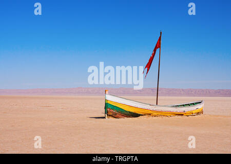 Kleine einsame Holzboot mit Red Flag in den Chott el Djerid endorheic Salt Lake mit bergkette am Horizont. Tunesien. Stockfoto