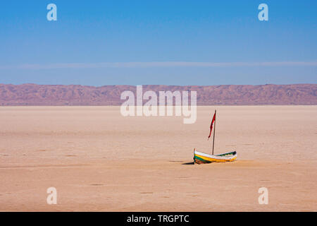 Kleine einsame Holzboot mit Red Flag in den Chott el Djerid endorheic Salt Lake mit bergkette am Horizont. Tunesien. Stockfoto