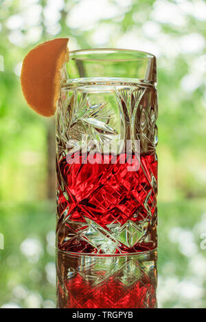 Kristallglas mit einem roten Cocktail und eine Zitronenscheibe auf der Terrasse im Sommer Stockfoto