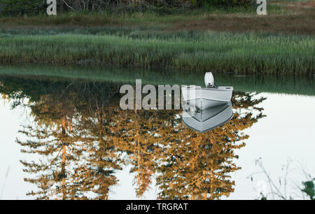 Ein kleines Motorboot in einem See hat eine Reflexion, die aussehen wie es auf einem Spiegel mit der Landschaft Reflexion ist zu ruhen. Stockfoto