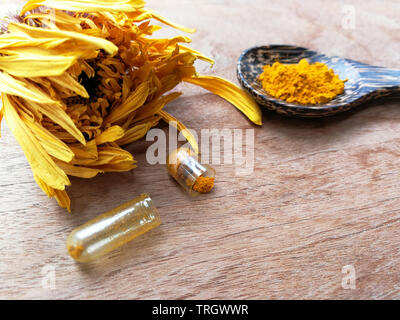 Natürliche Gelbwurzextrakt für Kraut Medizin Kapseln auf Löffel Blütenblätter calendula Gelb auf Holz- Hintergrund Stockfoto