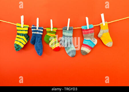 Mehrere Paare von bunte Wollsocken in verschiedenen Größen an einem Seil hängend mit weißem Hintergrund Stockfoto