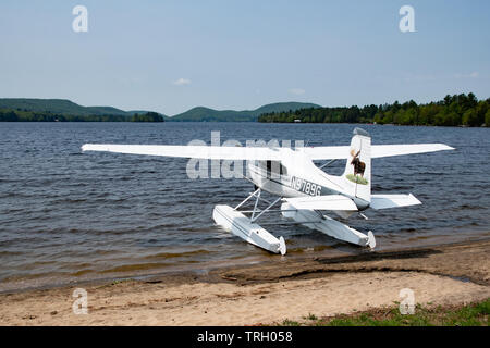 Eine Cessna 180 J Flugzeug mit Pontons am Strand geparkt auf See angenehm im Village Park in Spekulant, NY, USA Stockfoto