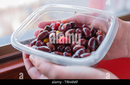 Kalamata oder Kalamon lila Griechische Oliven in einer Plastikschale mit zwei Händen gehalten werden. Frischen Aperitif, mit Olivenöl und leicht würzig Stockfoto