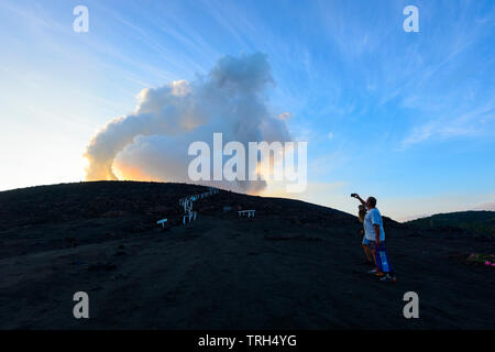Touristen, die auf den Hängen des ausbrechenden Mt Yasur Vulkan bei Sonnenuntergang, Insel Tanna, Vanuatu Stockfoto
