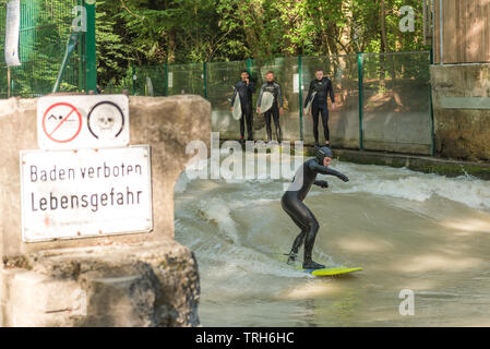 Männliche Surfer auf der Isar, der durch den Englischen Garten in München läuft, Deutschland mit Warnzeichen. Stockfoto