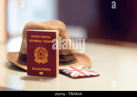 Einen italienischen Pass auf einem Glastisch zusammen mit einem Hut und ein Kartenlesegerät mit der Union Jack Flagge, Konzept Bild für eine Reise in das Vereinigte Königreich Stockfoto