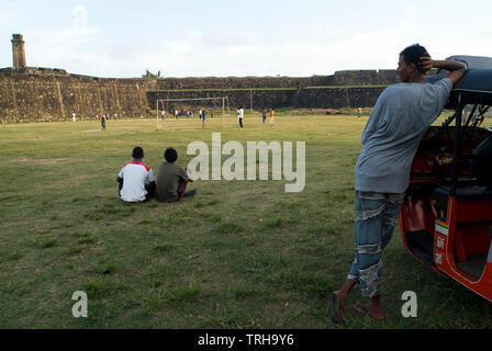 Ein Tuk Tuk Fahrer Uhren ein Cricket Spiel an der Galle International Stadium in Galle, Sri Lanka. Niederländische der Stadt erbaute Festung ist im Hintergrund zu sehen. Stockfoto