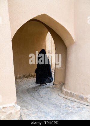 Eine Frau geht durch einen Torbogen in der Altstadt von Aqda, Iran Die Stadt wird derzeit für Tourismus restauriert. Stockfoto