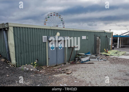 Run down Bürogebäude, aus grünem Wellblech, mit Müll und Schutt vor dem Gebäude. Und ein Riesenrad deutlich sichtbar hinter i Stockfoto