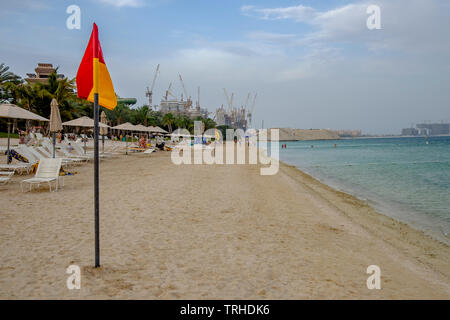 Ein Flag, am Ufer eines ruhigen Strand in Dubai, mit einem kleinen Meer Schiff in der Nähe der Küste verankert, an einem lauen Sommerabend Stockfoto