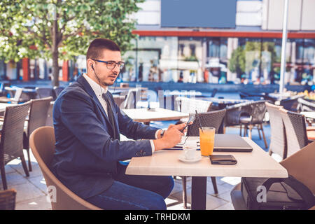 Junge Unternehmer in Video Anruf auf Smart Phone beim Trinken von Kaffee in Street Cafe Stockfoto