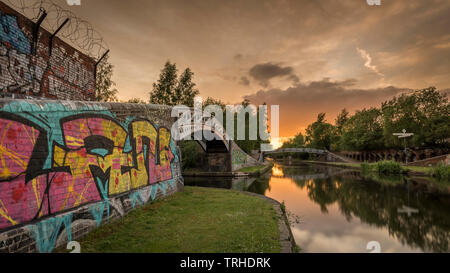 Spektakulären Sonnenuntergang über einem ruhigen Kanal, mit einem Graffiti überdachte Brücke im Vordergrund, und der Himmel im Wasser reflektiert Stockfoto